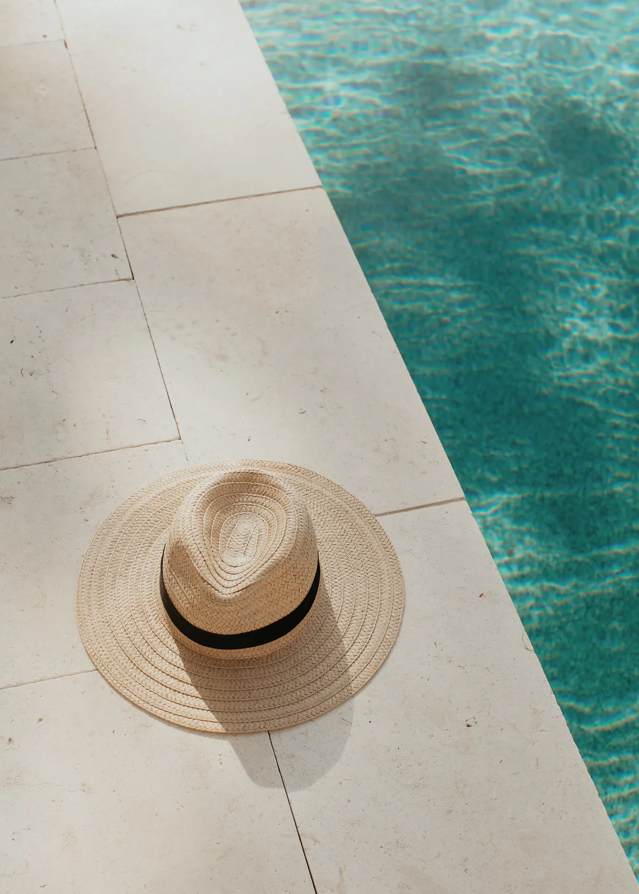 Straw sun hat resting on a stone pool deck beside clear turquoise water