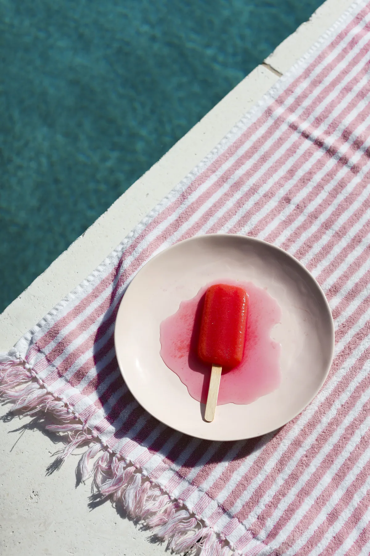 Melting fruit popsicle on a striped towel beside pool water