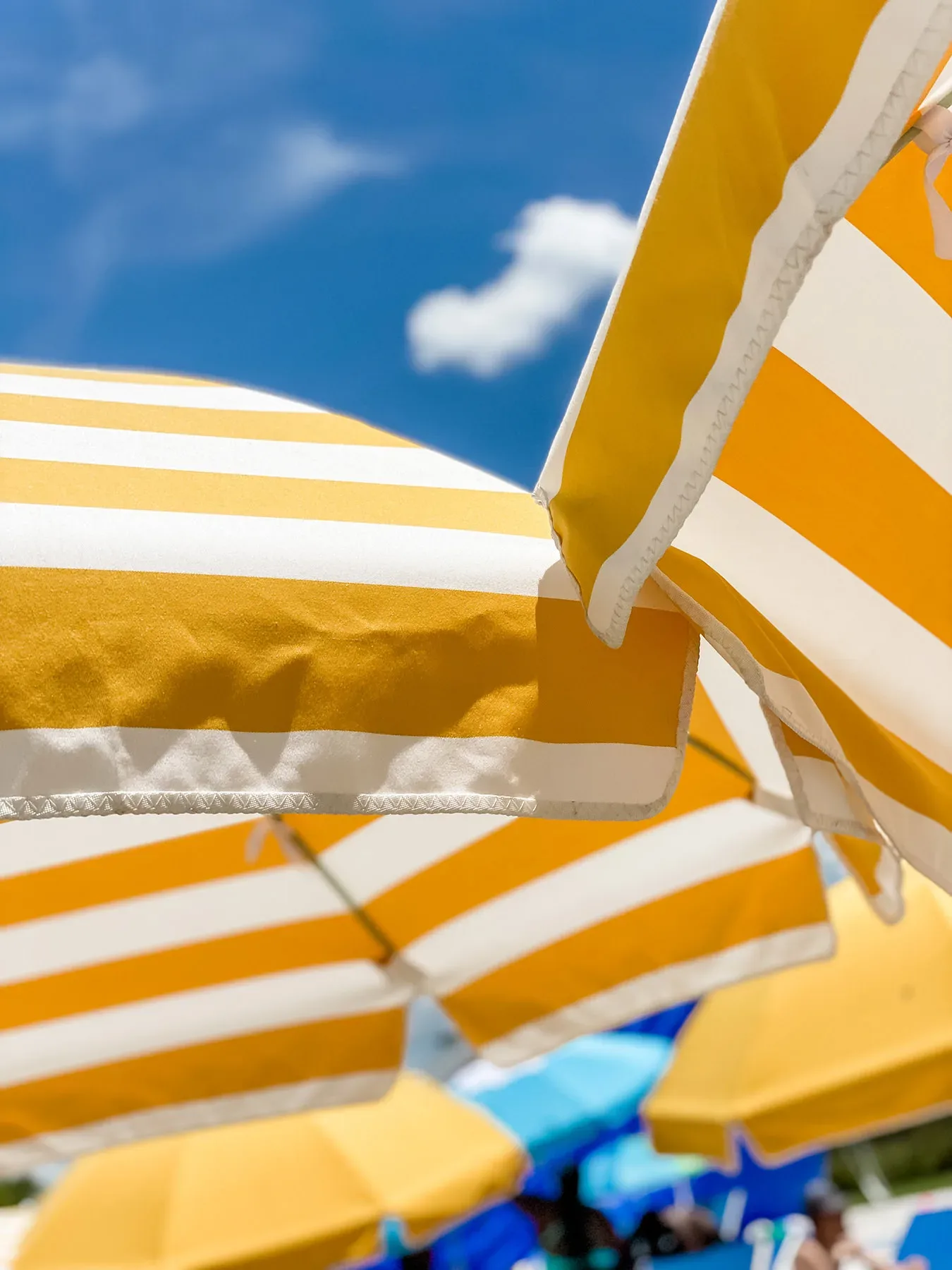 Marigold and white striped patio umbrellas against a bright blue sky