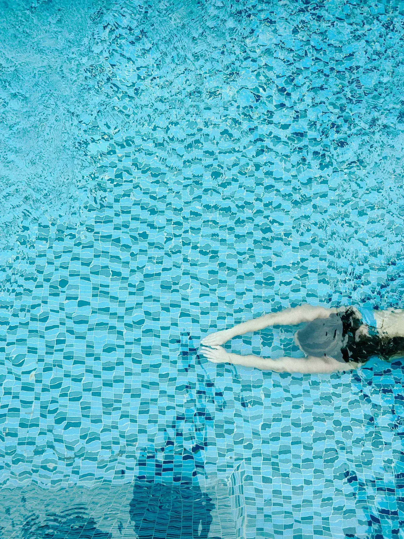 Overhead view of a swimmer gliding through crystal-clear blue pool water